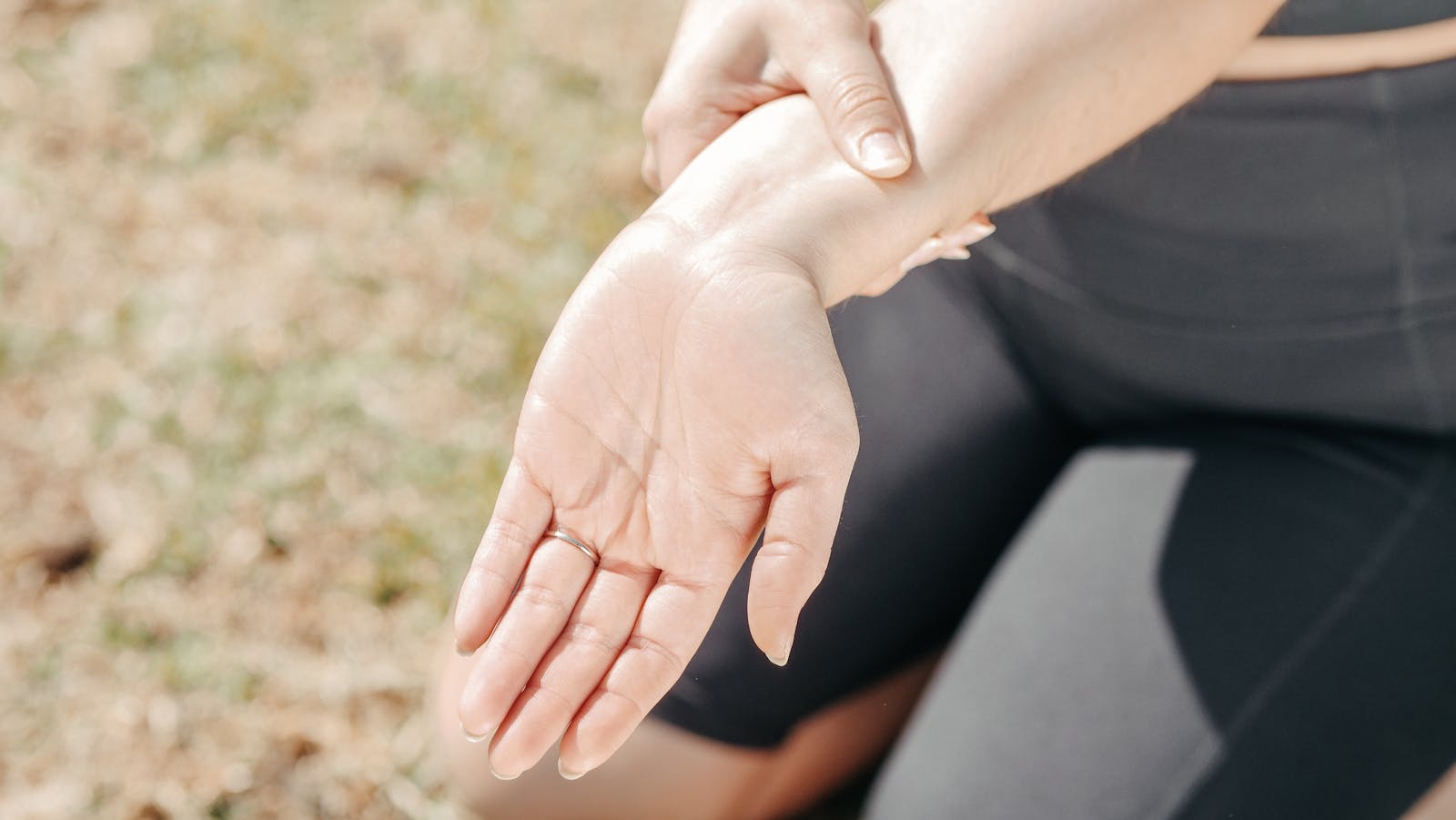 Person gripping wrist in pain, highlighting injury and support outdoors.